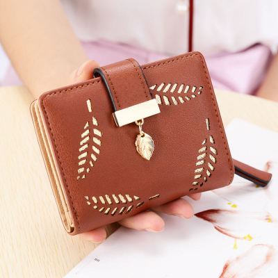 Brown wallet with leaf designs held by a person on a light background