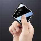 Hand holding a small power bank with a digital display on a dark background