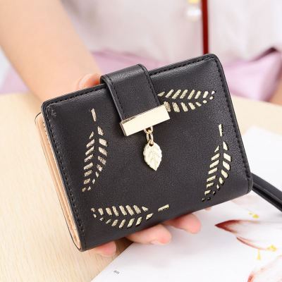 Black wallet with gold accents held by a person on a wooden surface.