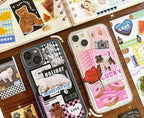 Two decorative smartphone cases displayed on a wooden surface with stickers and notebooks around them. 