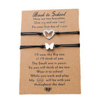 Two black cord bracelets with silver butterfly and heart charms displayed on a brown kraft paper card with printed sentimental text for a first day of school gift.