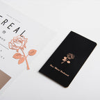 Black notebook with rose gold rose design and text on a white background