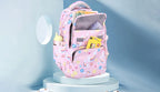 A pink patterned school backpack displayed on a light blue pedestal. The backpack has a pastel multicolor print and is shown filled with school supplies against a soft blue studio background.