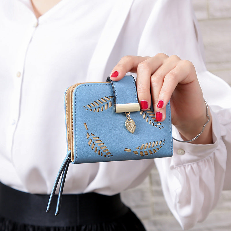 Hand holding a blue wallet with gold leaf designs against a white background