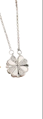 Silver four-leaf clover necklace on a display box with a gold necklace for comparison.