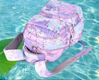 A pastel pink and purple water-resistant backpack with a floral and abstract print, shown on a turquoise water background.