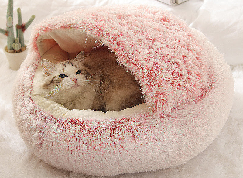 Cat lying in a pink plush pet bed on a white background.
