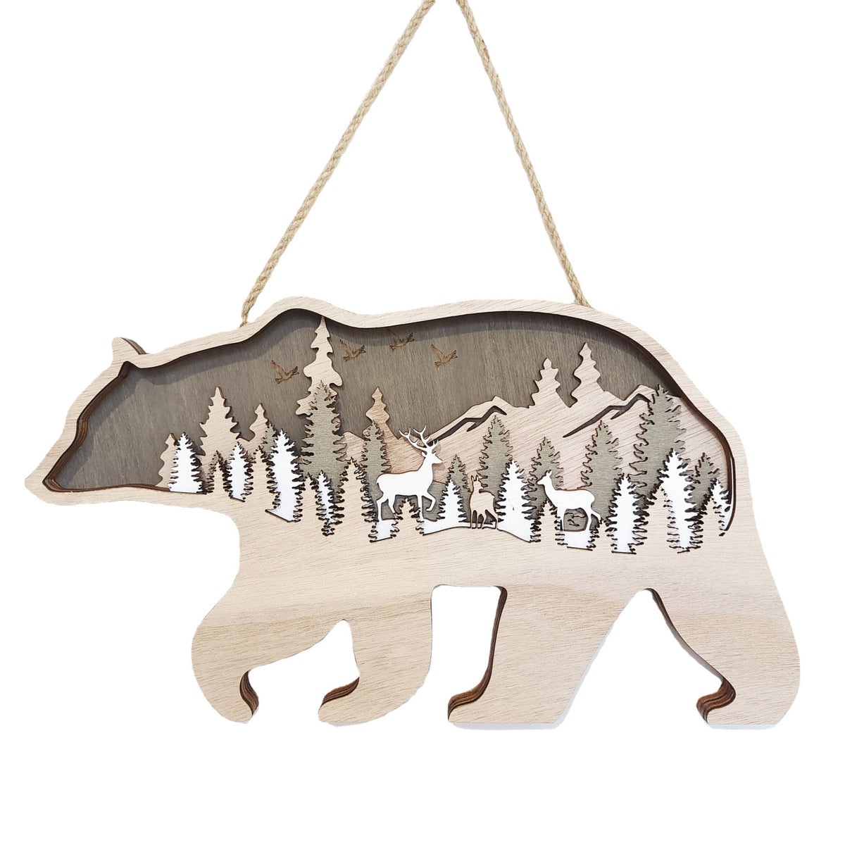A wooden hanging bear-shaped ornament featuring a laser-cut forest scene with pine trees, mountains, a deer, and birds. The ornament is made of light natural wood with a darker wood backing and hangs from a rope against a white background.