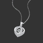 A silver heart-shaped pendant necklace with a central round clear gemstone and small accent stones along the edges, shown on a dark background.