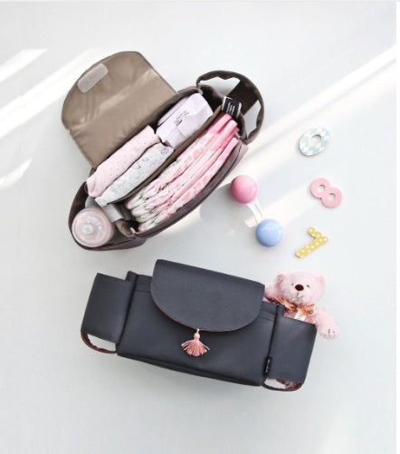 Black diaper bag with pink tassel on a white surface, containing baby items.