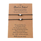 Two black cord bracelets with small silver heart charms displayed on a brown kraft card that reads 'Back to School' and includes sentimental text, photographed on a white background.