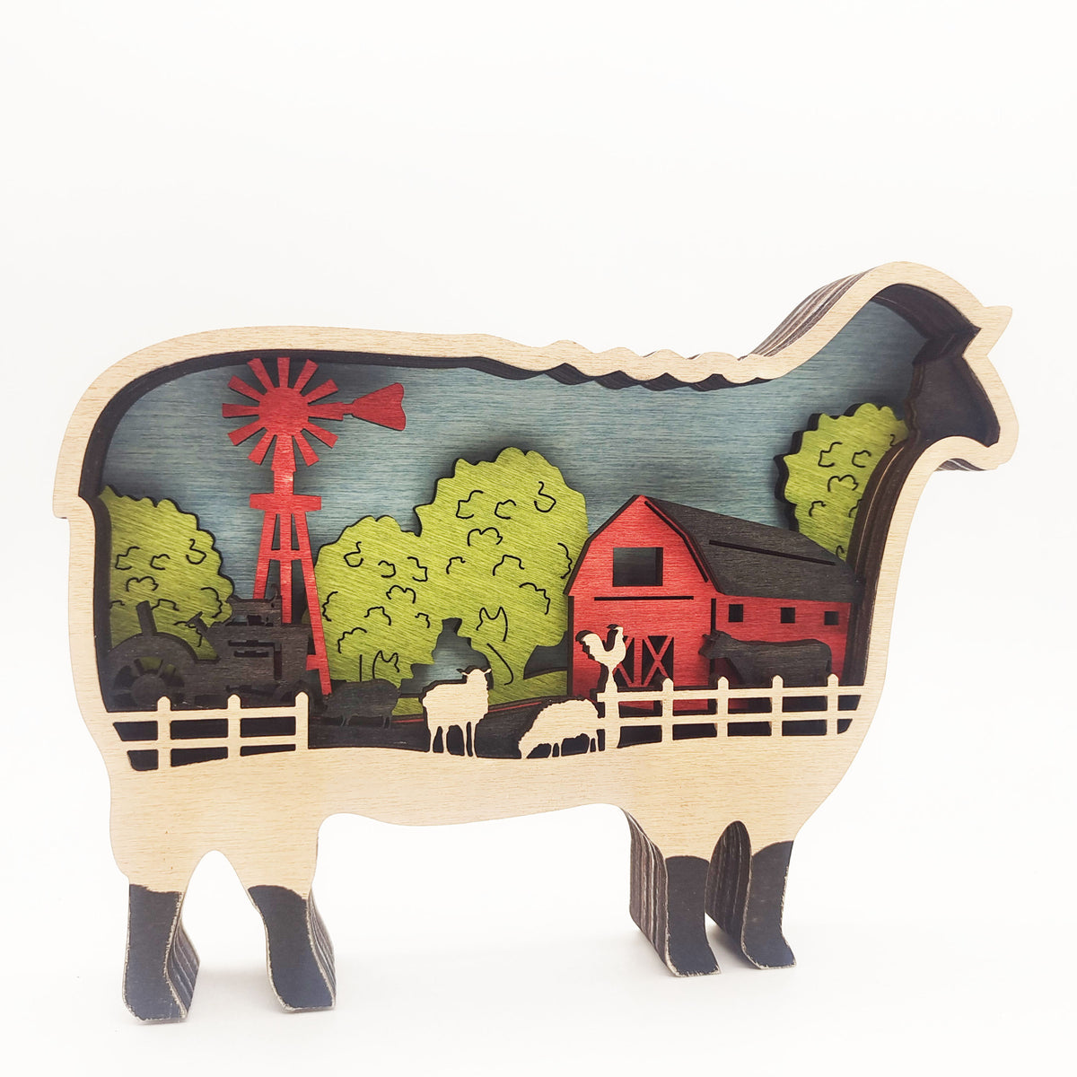 A wooden sheep-shaped decorative plaque featuring a colorful cutout farm scene with a red barn, red windmill, green trees, and small sheep figures, shown on a plain white background.