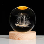 Crystal ball with ship engraving on a wooden base against a black background