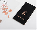 Black notebook with rose gold rose design on a white surface