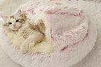 Cat lying in a fluffy pink pet bed on a soft surface.