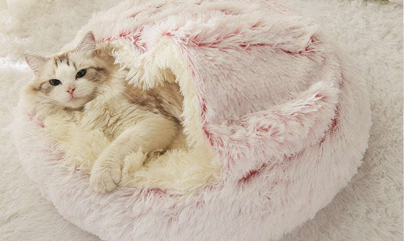 Cat lying in a fluffy pink pet bed on a soft surface.