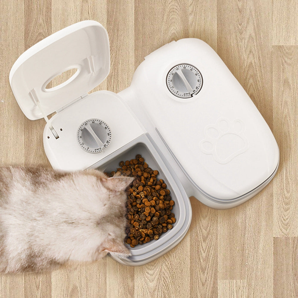 White pet food dispenser with cat eating from it on a wooden floor