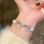 Silver bracelet with star and moon charms on a wrist against a blurred background
