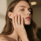Woman wearing a ring with a blue gemstone, touching her face.
