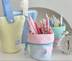 Colorful pencil holders with stationery items on a table next to a clock.