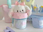 Cute plush toy with a pink bow inside a small bag on a desk with stationery items.