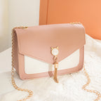 Pink handbag with gold chain and cat-shaped charm on a white surface.