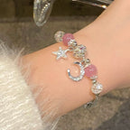 Bracelet with star and moon charms on a wrist against a neutral background