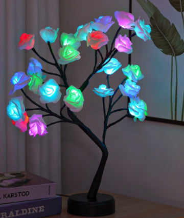 Colorful LED tree lamp on a stand with books and a plant in the background
