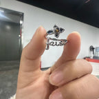Silver ring with floral design and 'faith' engraving held by a hand against a blurred indoor background.