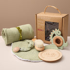 Baby care products including a green blanket, teether, and wooden items on a beige surface with a brown box in the background.