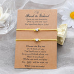 Two heart-shaped bracelets on a card with a message, placed on a textured surface with flowers in the background.