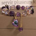 Bracelet with purple beads and a heart-shaped crystal charm on a wooden surface.