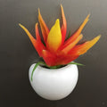 Artificial plant with orange and yellow leaves in a white pot on a dark background