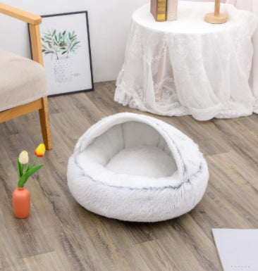 White pet bed on a wooden floor with a small table and plant in the background