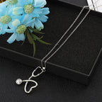 Silver stethoscope-shaped pendant necklace on a black display box with blue flowers.