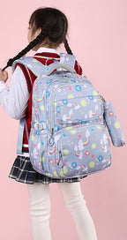 A child model shown from the back wearing a light blue unicorn-print backpack with a matching shoulder bag, set against a pink background.