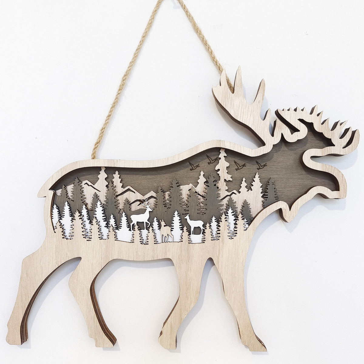 A wooden moose-shaped hanging ornament with a laser-cut forest and deer design inside, suspended by a natural jute rope against a plain white background.